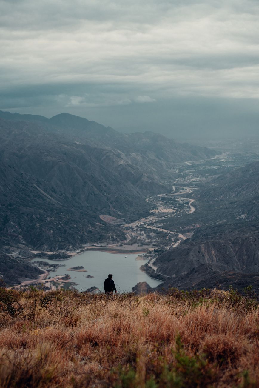 Person stands overlooking the dramatic mountainous landscape of La Rioja, Argentina under a cloudy sky.
