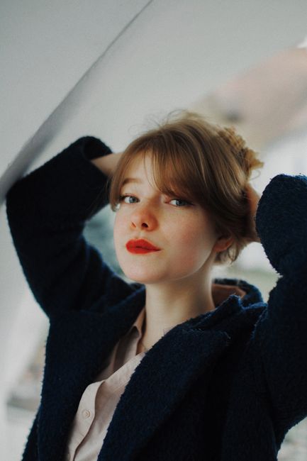 Stylish portrait of a young woman with red lipstick and a blue coat indoors.