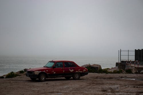 Red Car on Sand Near Body of Water