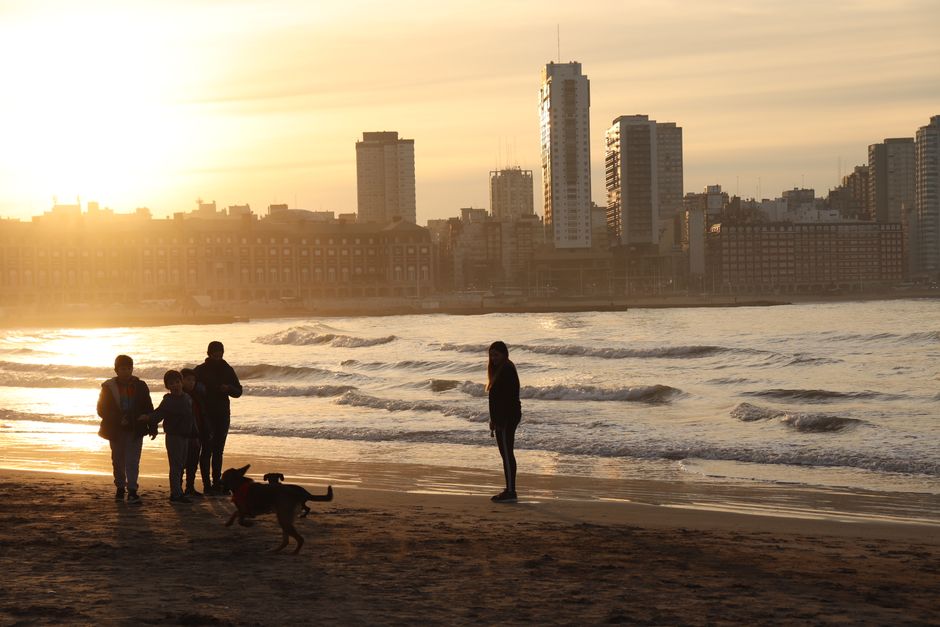 Family enjoying a sunset walk on Mar del Plata beach with city skyline in the background.