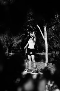Monochrome photo of a woman athlete with hockey stick outdoors.