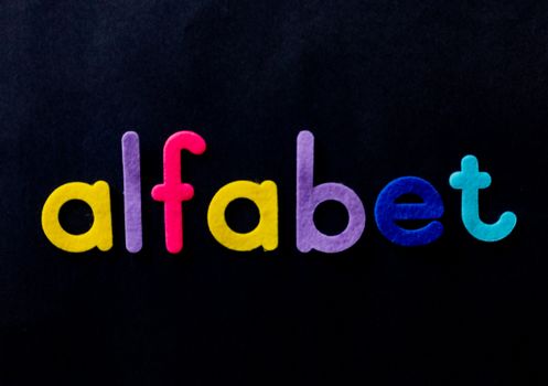 Brightly colored alphabet letters spelling 'alfabet' on a black surface, ideal for educational themes.