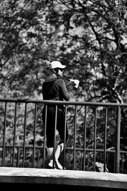 Free A woman standing on a bridge holding a badminton racket in a black and white photo. Stock Photo