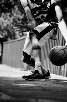 Black-and-white photo of a man playing basketball outdoors, focusing on action and movement.