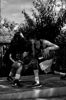 Intense black and white image capturing two athletes playing basketball outdoors with high energy.