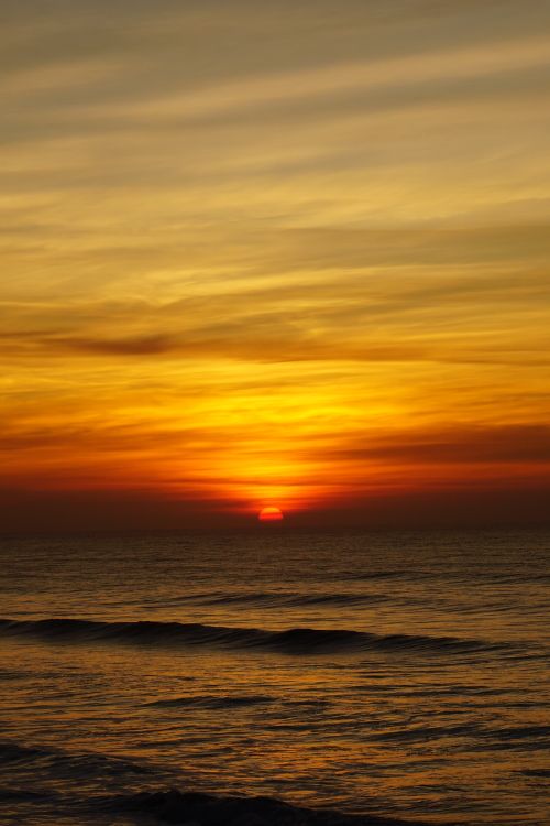 Free Capture the tranquil beauty of an ocean sunset with a vibrant golden sky casting over gentle waves. Stock Photo