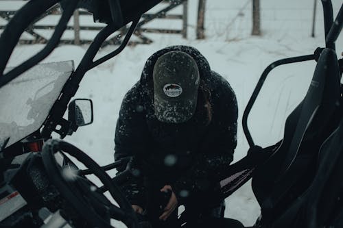 A Person in Black Winter Jacket and Black Cap About to Enter a Vehicle