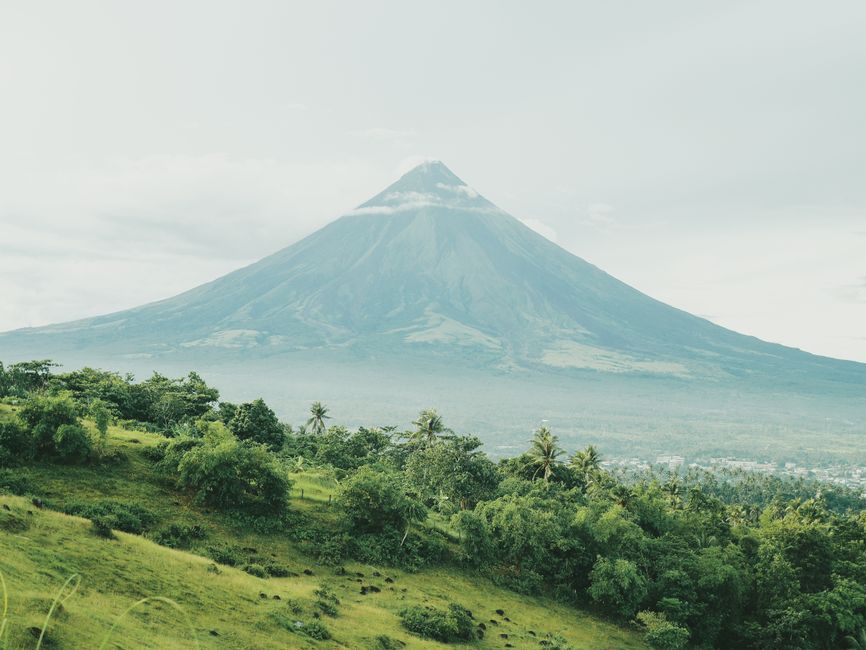 Serene landscape of Mayon Volcano surrounded by lush vegetation under a cloudy sky.