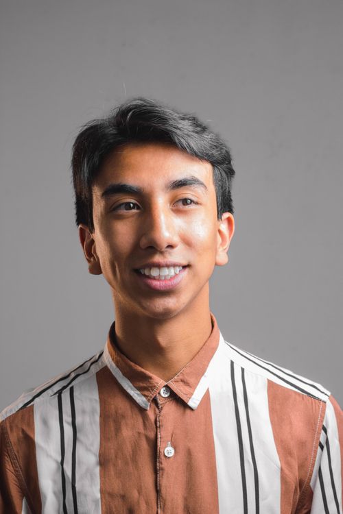 Free Portrait of a smiling young man wearing a striped shirt against a gray background. Stock Photo