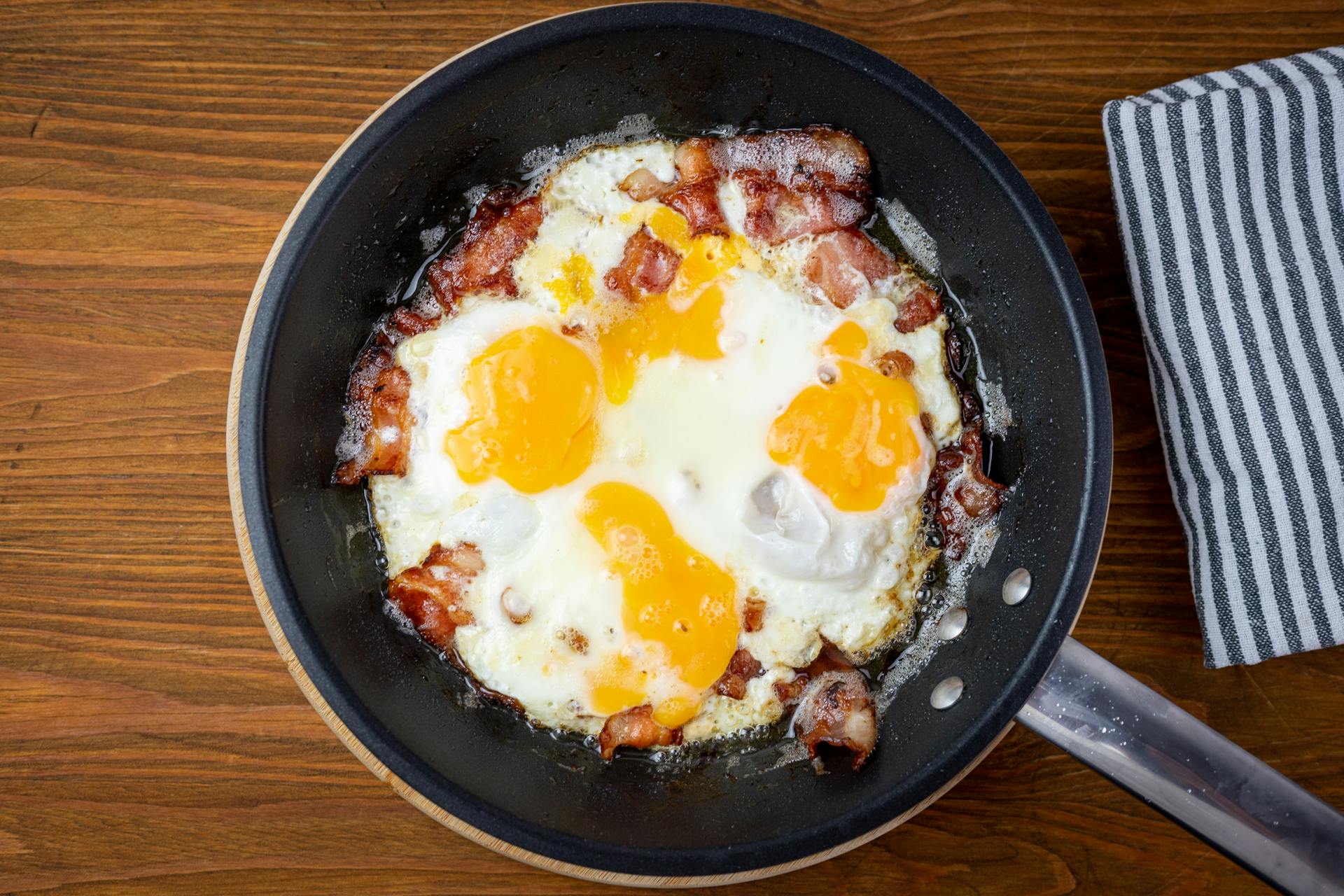 Sizzling bacon and sunny side up eggs in a frying pan, perfect for breakfast lovers.