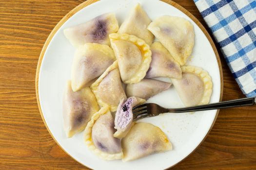 Delicious homemade blueberry dumplings on a white plate with a fork and checkered cloth.