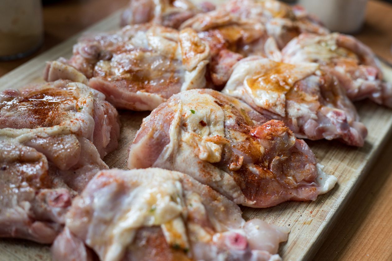 Raw chicken pieces seasoned with jerk spice paste on a wooden cutting board