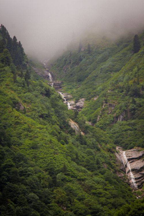 Free A serene view of mist-covered green mountains with cascading waterfalls, enhancing the natural landscape. Stock Photo