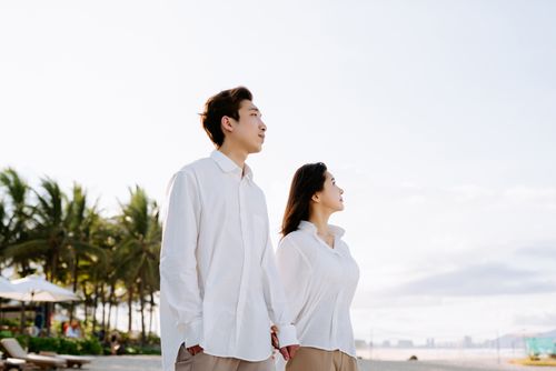 Free Asian couple enjoying a sunny day on a tropical beach, holding hands and gazing forward. Stock Photo