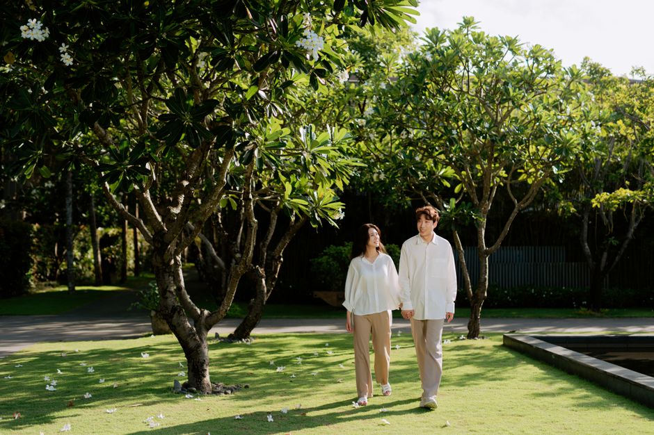A happy Asian couple holding hands and walking together in a sunlit park.