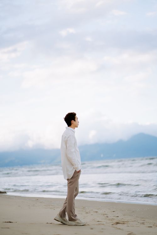 Free A man enjoys a relaxing walk on a tranquil beach at sunset. Stock Photo