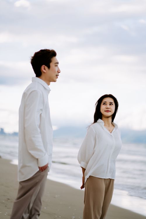 Free An Asian couple enjoys a peaceful walk on the beach, exuding romance and tranquility. Stock Photo