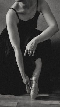 Elegant black and white photo of a ballerina adjusting her pointe shoes with graceful poise.