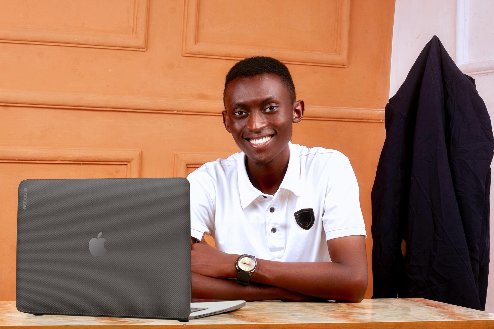 Young African man smiling at a desk with a laptop, in an office setting.