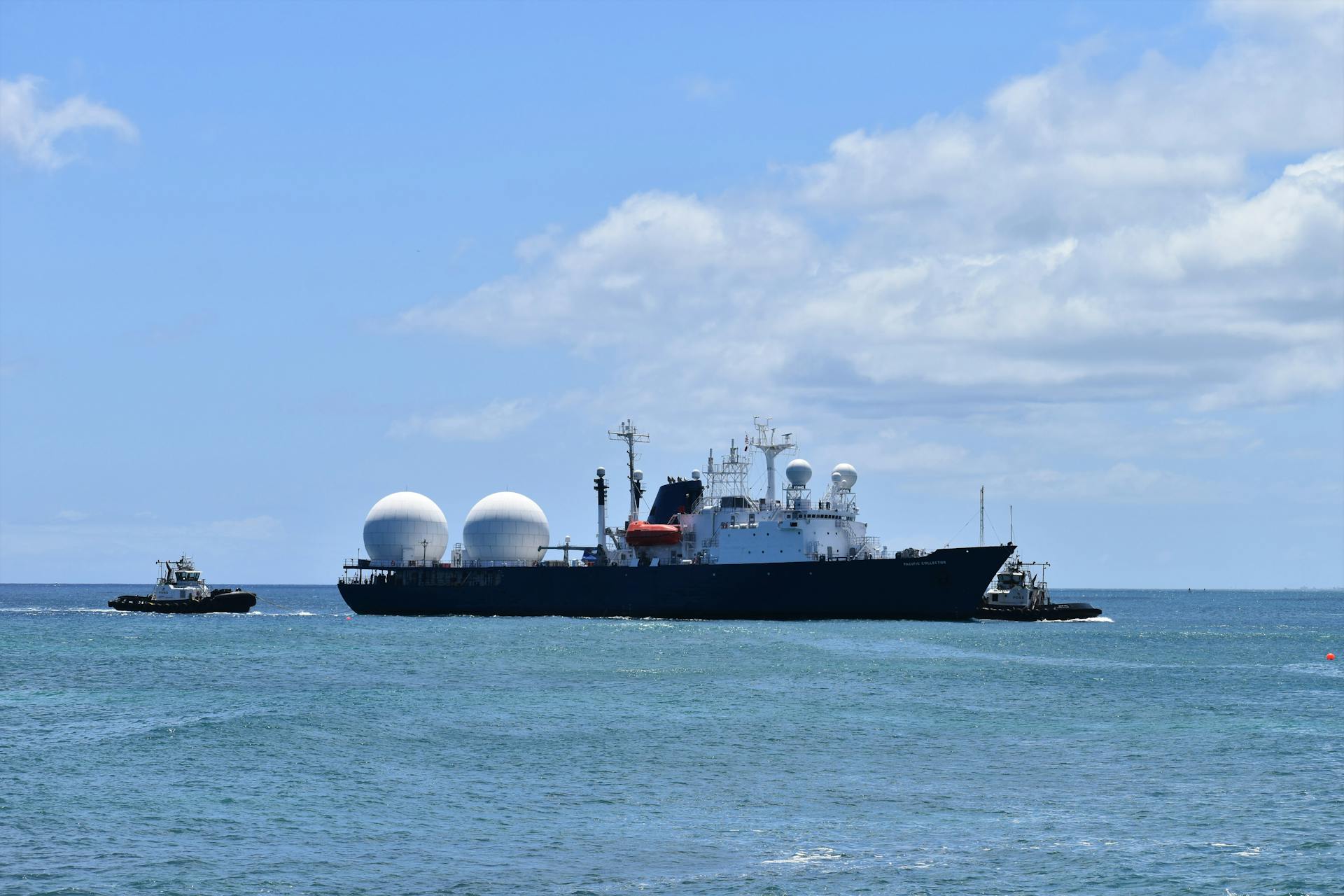 A large industrial ship escorted by a tugboat sailing on the ocean under a clear sky.