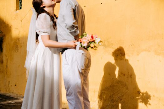 A bride and groom embrace romantically, casting a loving shadow on a sunlit wall.
