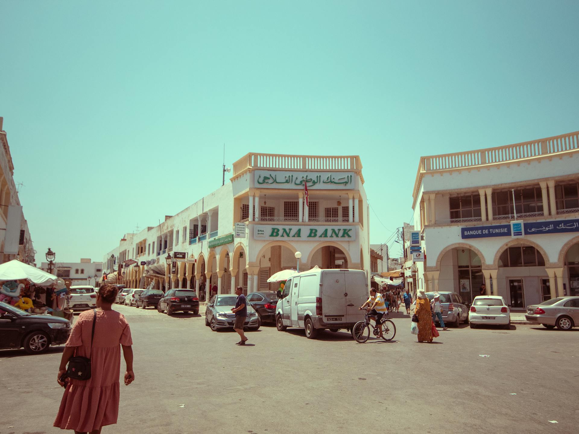 A lively street scene in Tunis featuring the iconic BNA Bank and local people walking or biking.