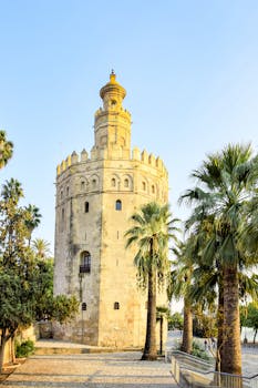 Historic Torre del Oro in Sevilla, Spain surrounded by lush palm trees on a sunny day.