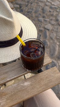 Refreshing iced drink with straw and hat on a wooden bench, capturing a summer's day in Ayvalık.