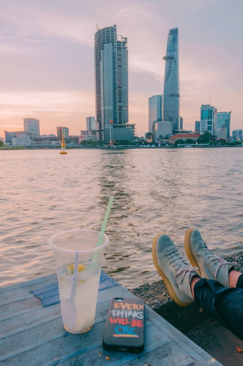 Person Sitting Beside Table Near Body of Water and Buildings