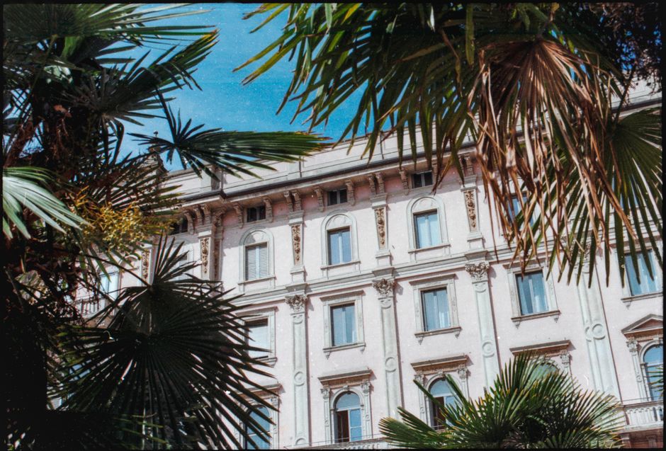 A stunning view of a historic Milanese building framed by lush palm trees under a bright blue sky.