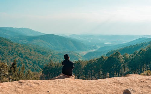 Человек, сидящий на скале с видом на гору