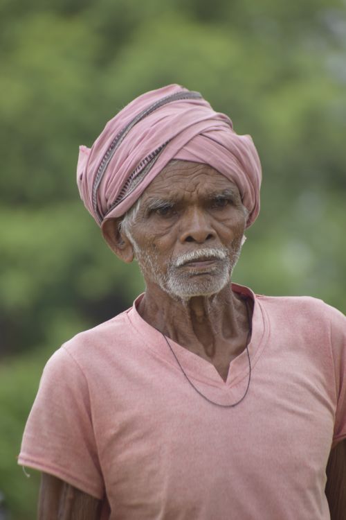 Free Portrait of an elderly man wearing a pink turban and shirt, captured outdoors. Stock Photo