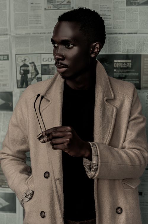 Free Fashionable African American man in a coat holding sunglasses with a newspaper backdrop. Stock Photo
