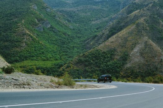 A black car navigating a winding road through lush green mountains, perfect for travel themes.