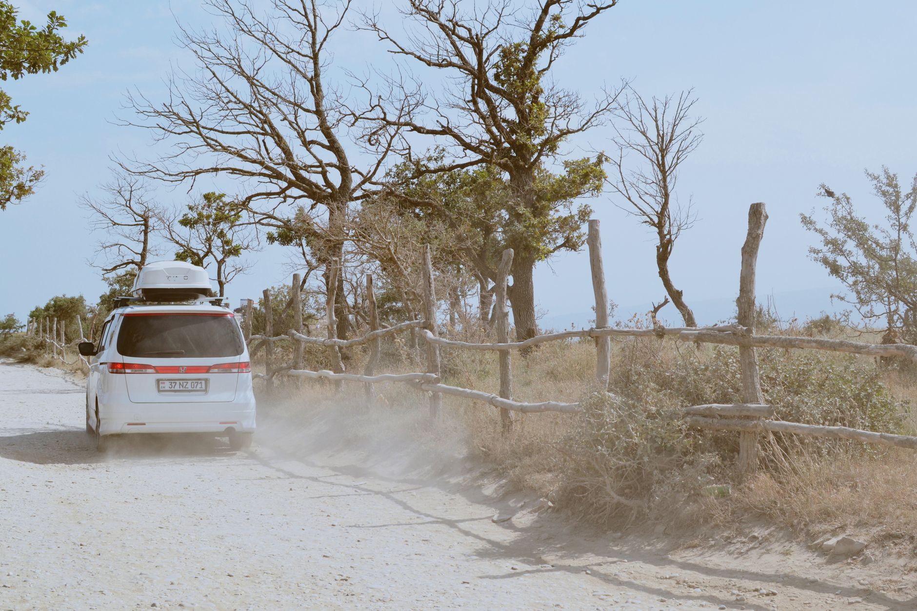 White SUV driving along a dusty dirt road surrounded by trees on a sunny day; perfect for travel enthusiasts.