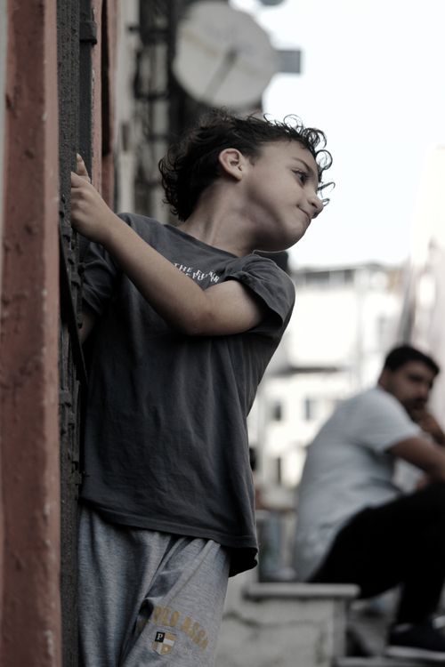 Free Young child peeping around a city building, evoking curiosity and playfulness. Stock Photo