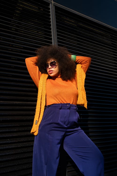 Woman with Afro Hairstyle Posing in Orange Blouse against Metal Wall