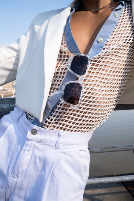 Close-up of a model in a net blouse, white jacket, and sunglasses in fashion photography.