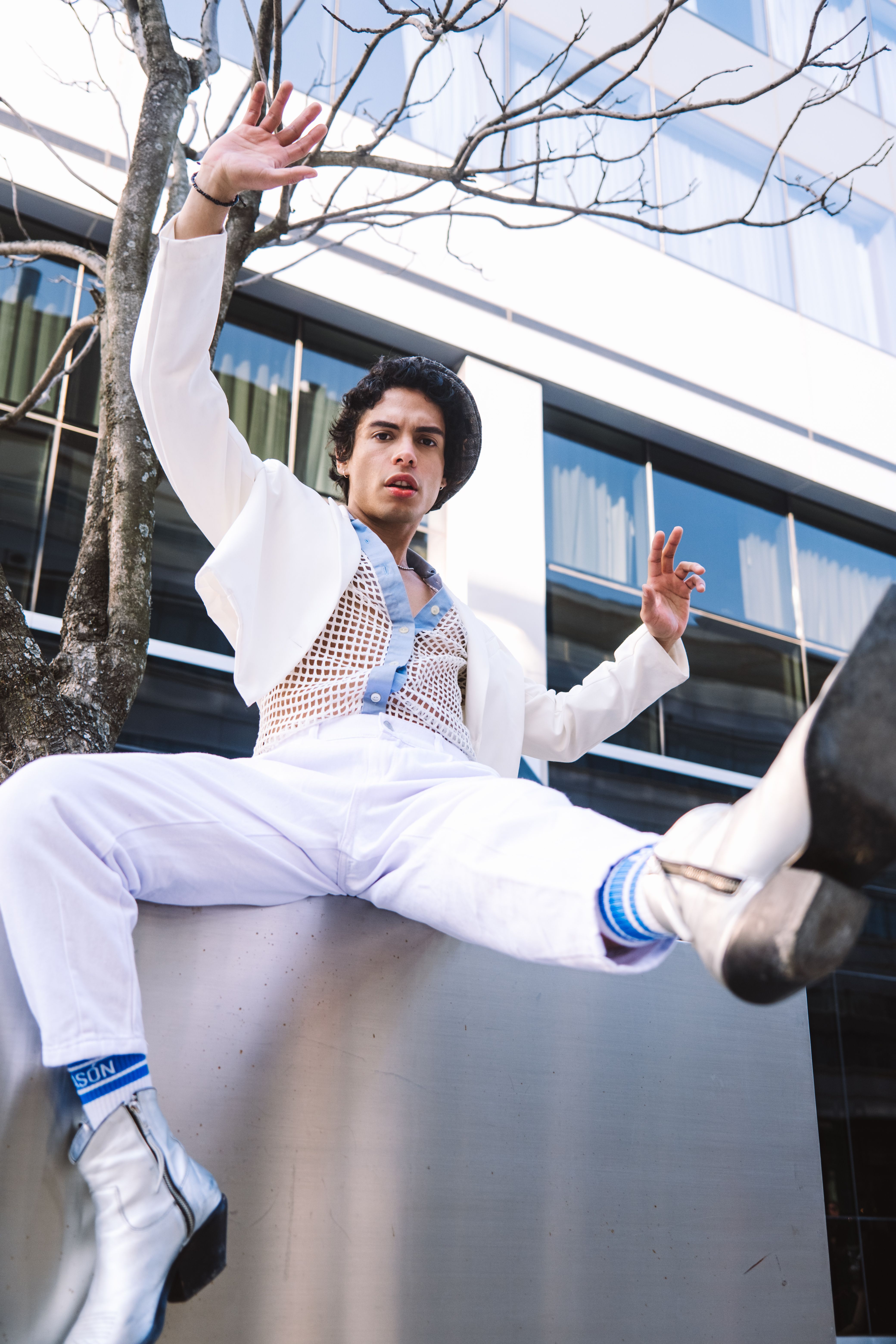Stylish man in white outfit posing playfully in a modern cityscape.