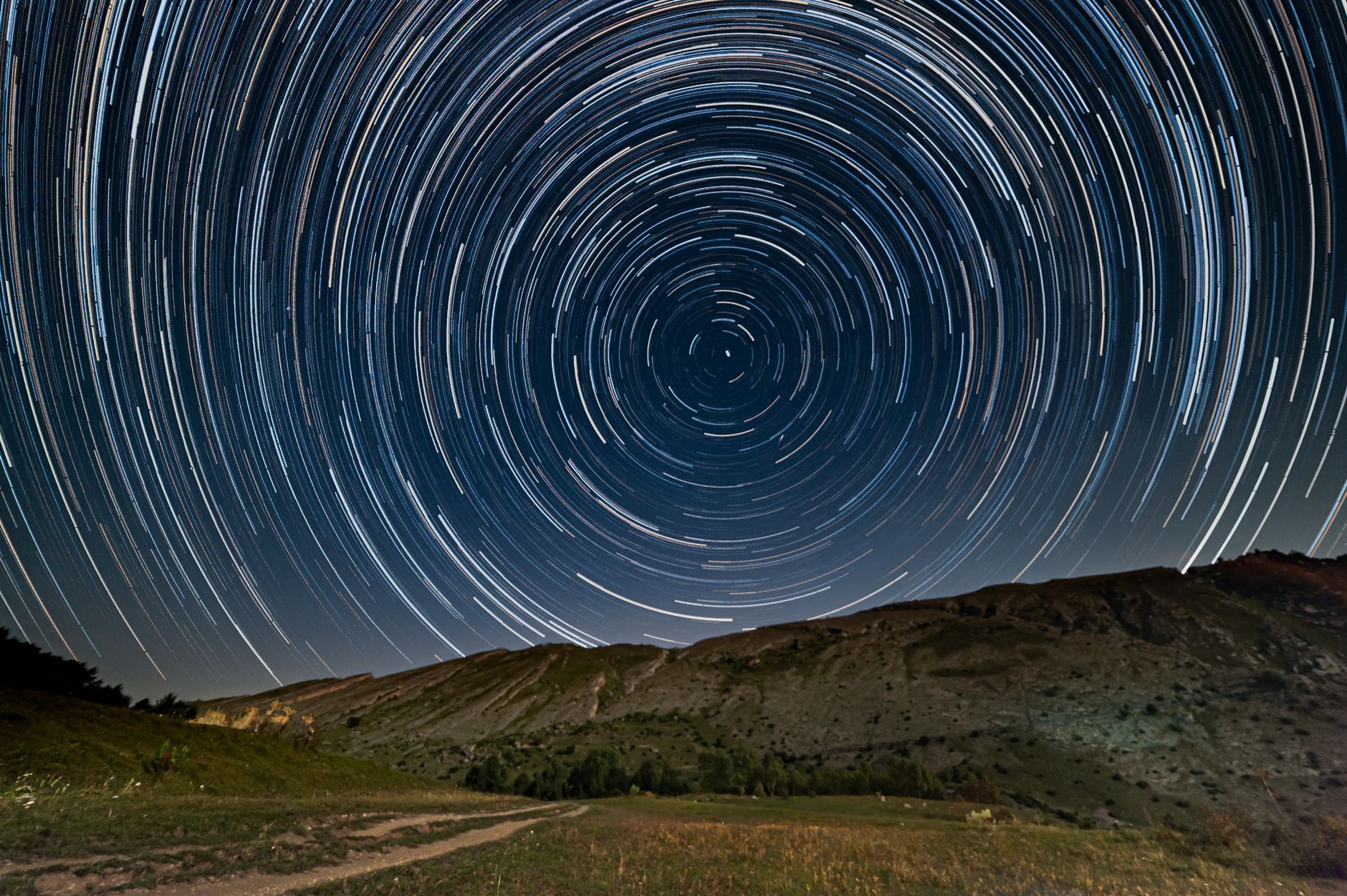 Captivating star trails forming circles above a serene mountain scene, captured with long exposure.