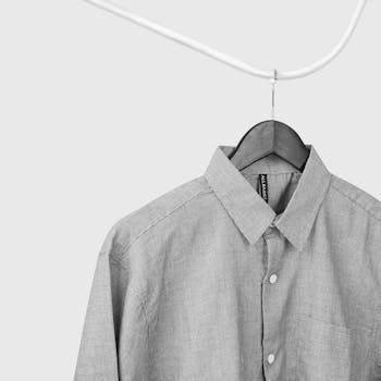 Close-up of a gray button-up shirt hanging on a wire hanger against a white wall.