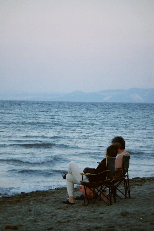 Couple Relaxing and Sitting on a Folding Chairs in Front of a Sea