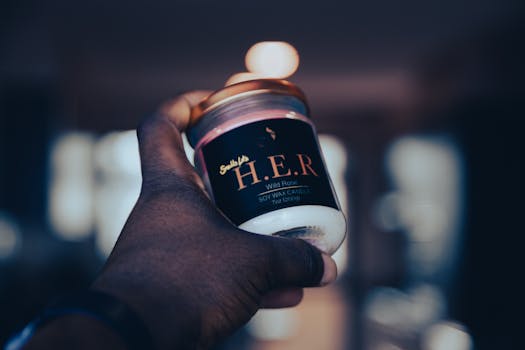 Close-up of a hand holding a soy wax candle indoors, perfect for relaxation.