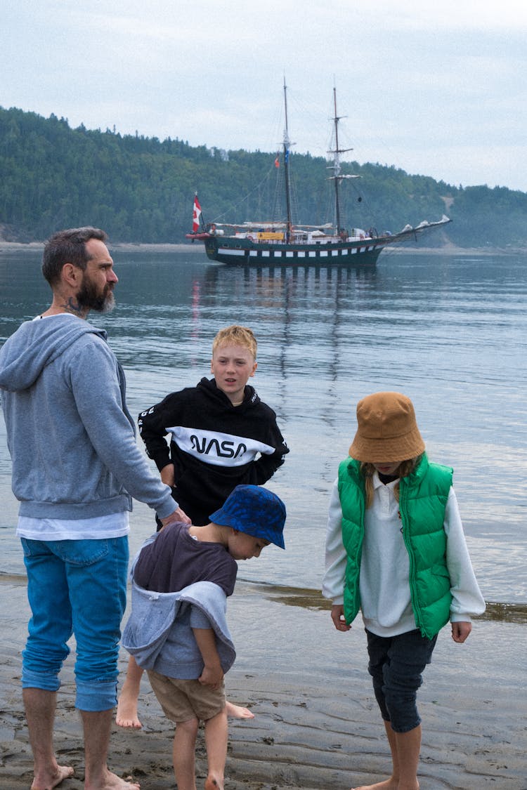 A Family Standing On The Beach With A Boat On The Water