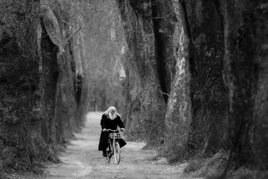 A senior man with a beard cycling through a tree-lined path in winter.