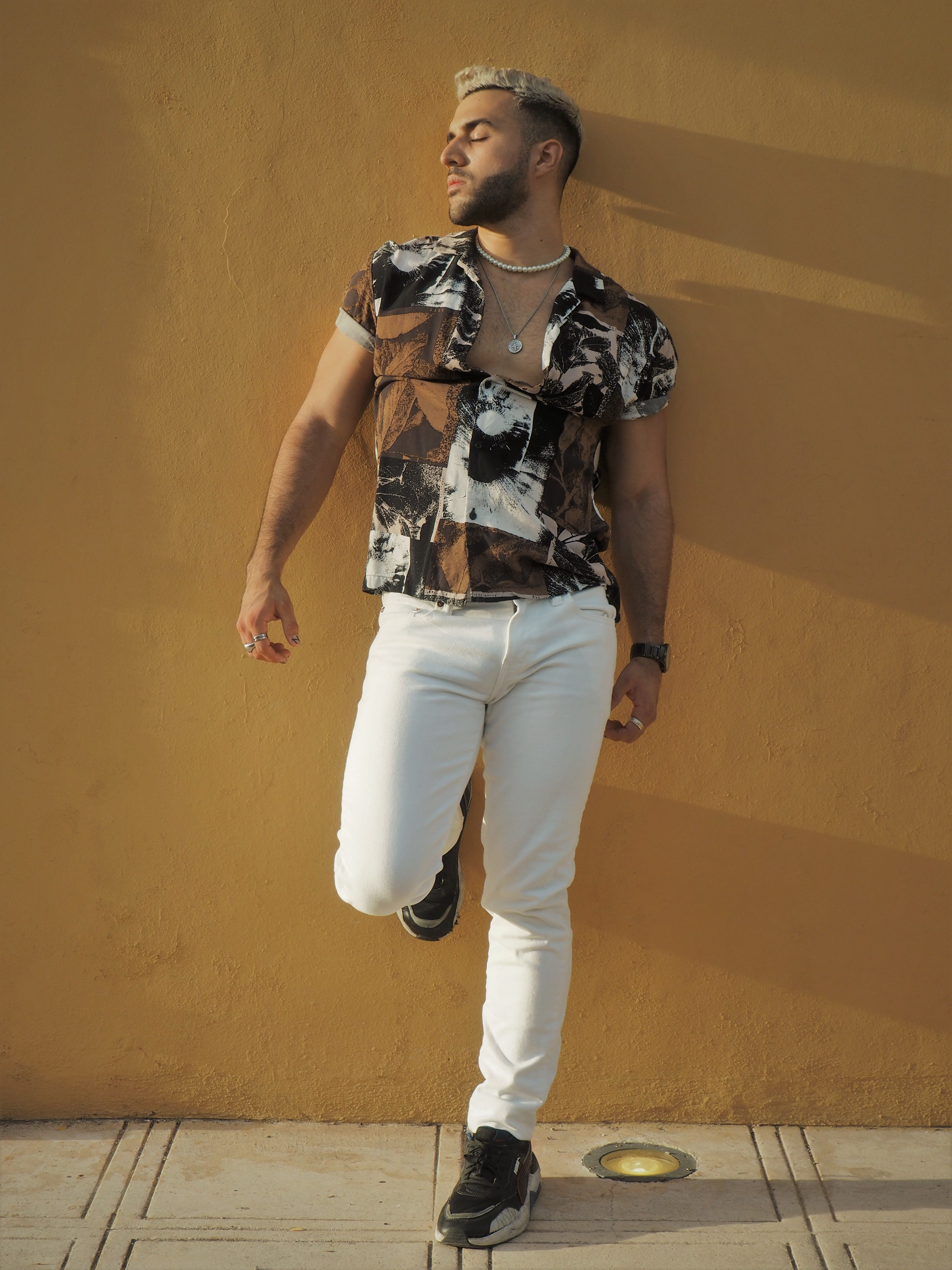 Fashionable man leans against a sunlit yellow wall in Mérida, showcasing modern style.