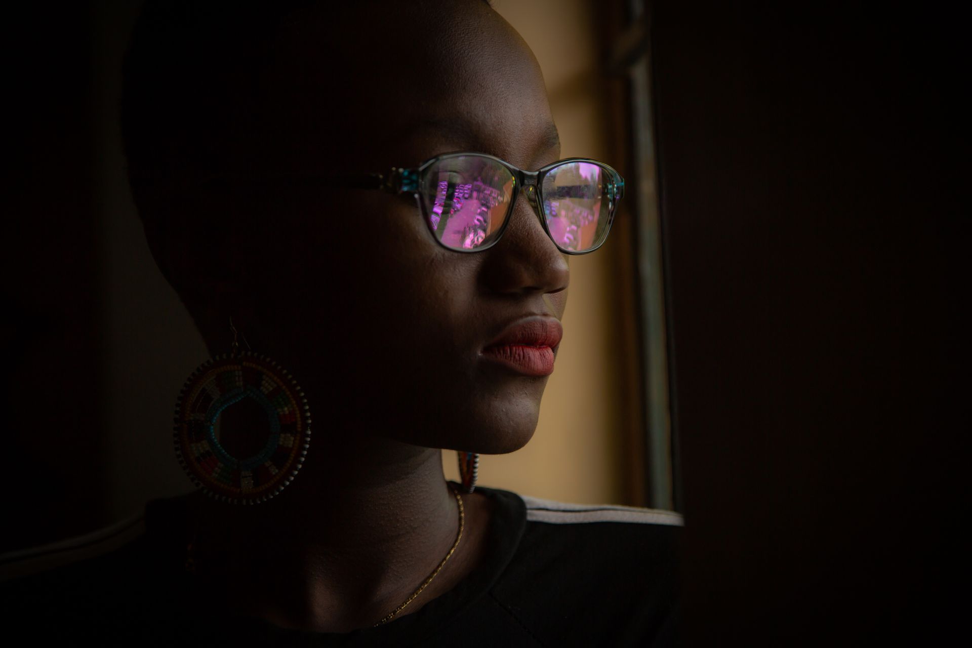 Portrait of a woman with glasses and colorful earrings gazing out a window.