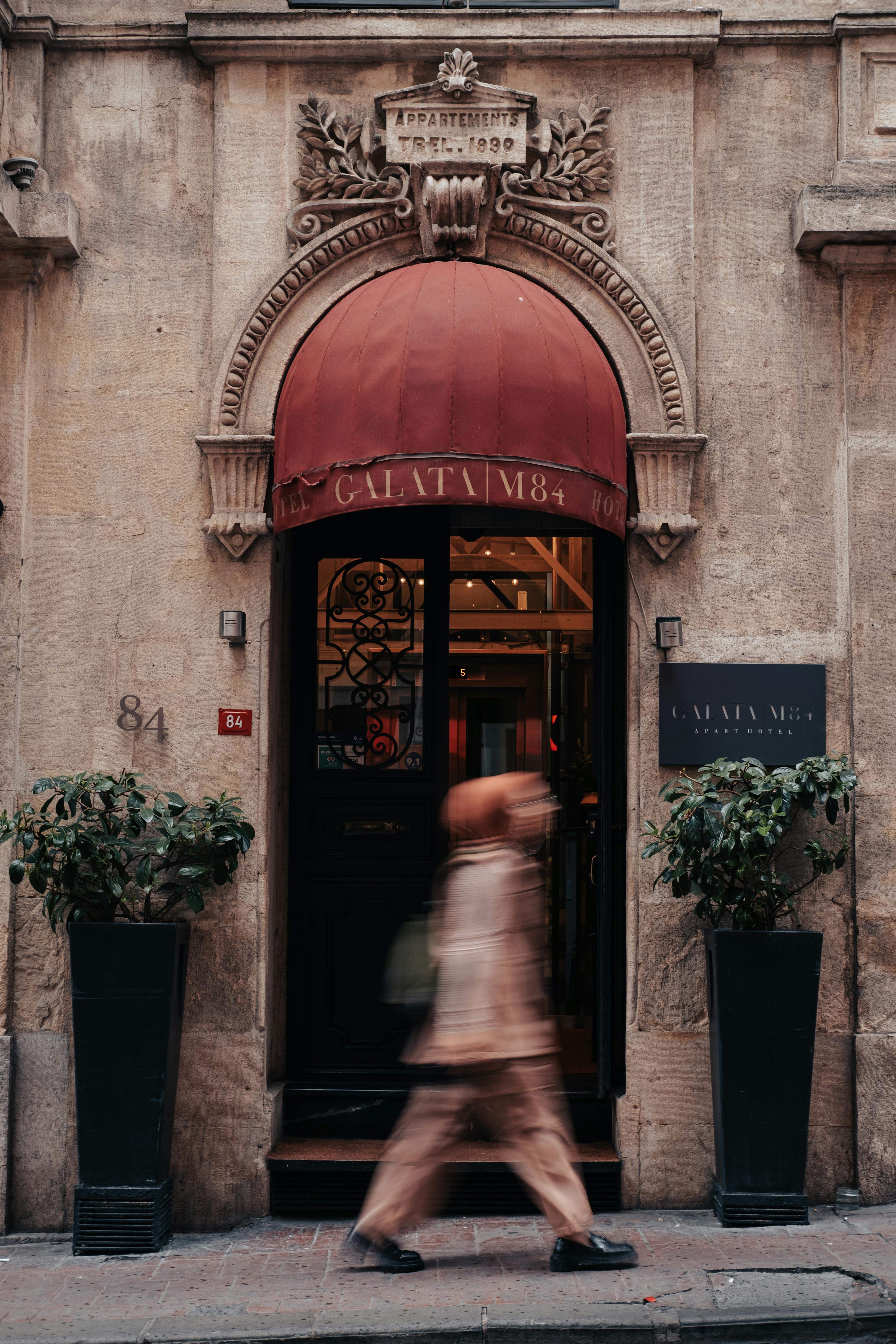 Blurred pedestrian passes a classic urban entrance with ornate details and red awning.