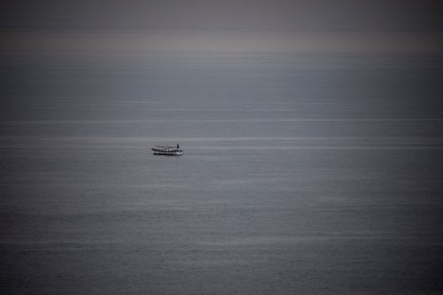 Free A solitary boat drifts on an expansive ocean, creating a serene seascape with moody tones. Stock Photo