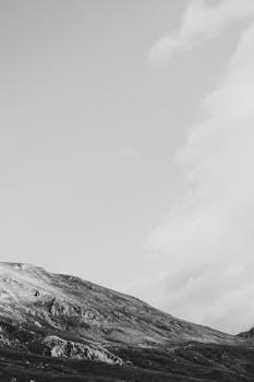 A serene grayscale landscape of a rocky mountain slope beneath a vast cloudy sky.